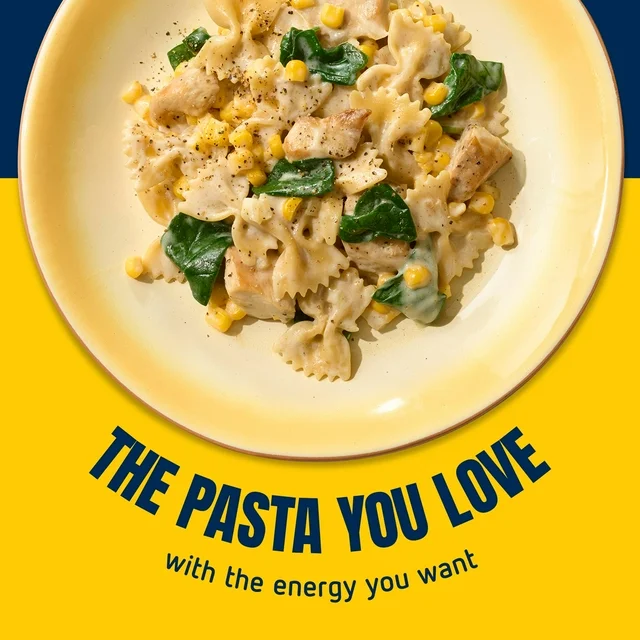 Pasta dish with chicken, spinach, and corn on a yellow plate with blue background